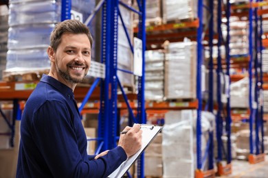 Photo of Happy manager holding clipboard in warehouse with lots of products. Space for text