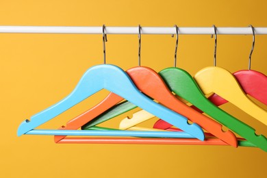 Bright clothes hangers on metal rail against yellow background