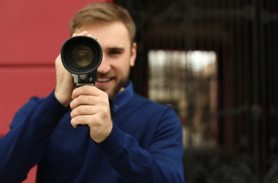 Young man using vintage video camera outdoors, focus on lens. Space for text