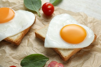 Photo of Heart shaped fried eggs with toasts, spinach and tomatoes on white wooden table, closeup