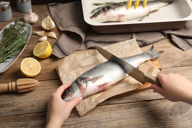 Photo of Woman cutting raw sea bass fish at wooden table, closeup