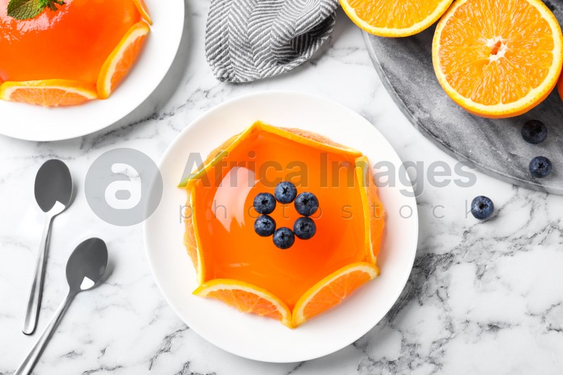 Delicious fresh jelly with orange slices and blueberries on marble table, flat lay