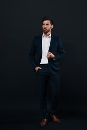 Handsome bearded man in suit looking away on black background