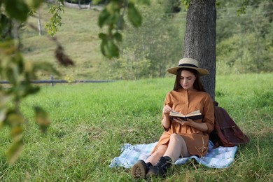 Young woman reading book under tree on meadow
