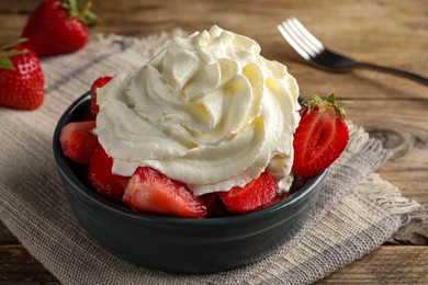 Bowl with delicious strawberries and whipped cream served on wooden table, closeup