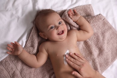 Mother applying moisturizing cream onto her little baby's skin on towel, closeup