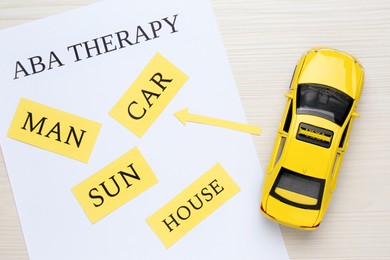 Taxi car model near sheet of paper with text ABA Therapy and different words on white wooden table, flat lay. Applied behavior analysis