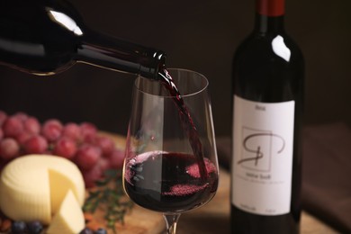 Photo of Pouring red wine into glass and appetizers on table, closeup