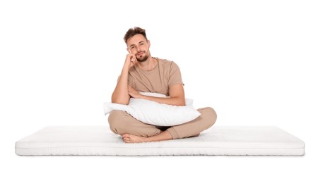 Man with pillow sitting on soft mattress against white background