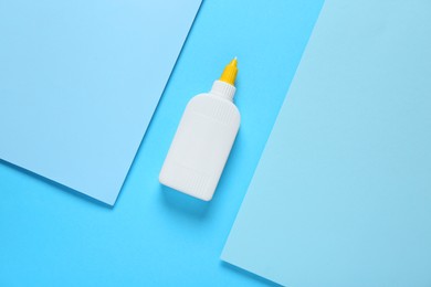 Bottle of glue and paper on light blue background, flat lay