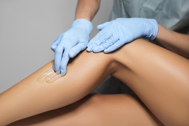 Photo of Young woman undergoing hair removal procedure on legs with sugaring paste in salon, closeup