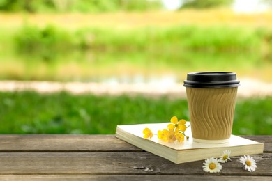 Paper coffee cup, flowers and book on wooden table outdoors, space for text