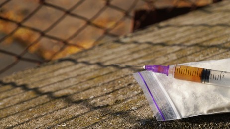 Photo of Plastic bag with powder, syringe on stone surface outdoors, closeup and space for text. Hard drugs