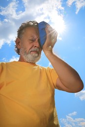 Senior man with cold pack suffering from heat stroke outdoors, low angle view