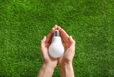 Woman holding LED light bulb over green grass, top view