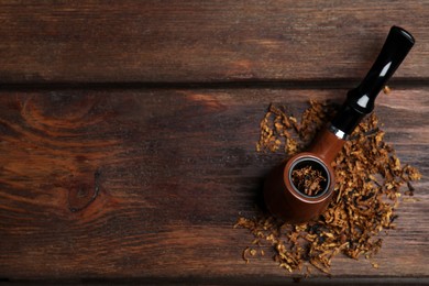 Smoking pipe and dry tobacco on wooden table, flat lay. Space for text