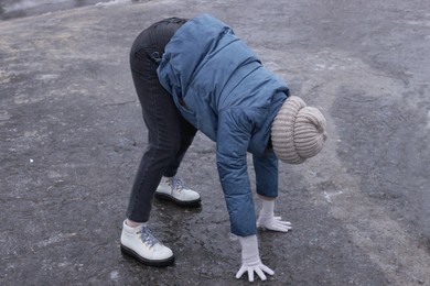 Young woman having difficulties with moving on icy road outdoors