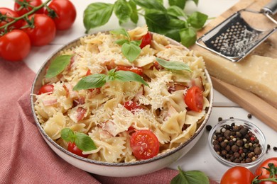 Photo of Plate of delicious pasta with tomatoes, basil and parmesan cheese near ingredients on white table