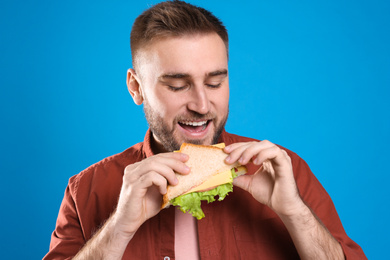 Photo of Young man eating tasty sandwich on light blue background