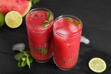 Glasses of delicious fresh watermelon juice, lime, mint and ice on black wooden table