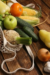 Different fresh vegetables in net bag on wooden table, closeup. Farmer harvesting