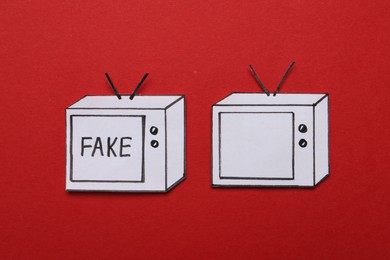 Photo of Paper TVs with word Fake and empty screen on red background, flat lay. Information warfare concept