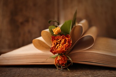 Open book with folded pages and beautiful dried flowers on wooden table, closeup