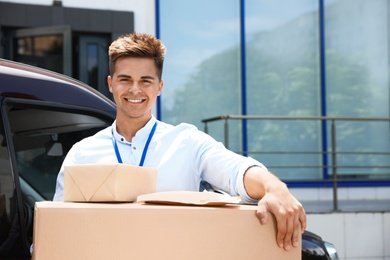 Young courier with parcels near delivery car outdoors