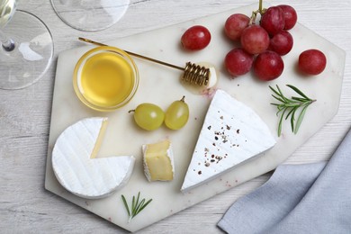 Tasty brie cheese with honey, rosemary and grapes on white wooden table, flat lay