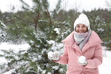 Beautiful young woman with snowballs in winter forest