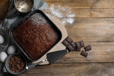 Photo of Homemade chocolate sponge cake and ingredients on wooden table, flat lay. Space for text
