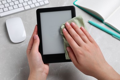Woman wiping smartphone with paper at gray marble table, closeup