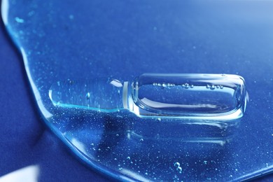 Pharmaceutical ampoule with medication in transparent gel on blue background, closeup
