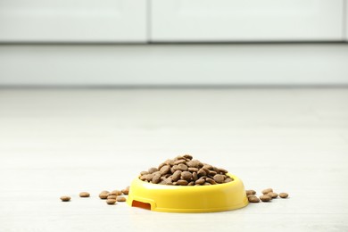 Photo of Bowl with dry dog food on white floor indoors