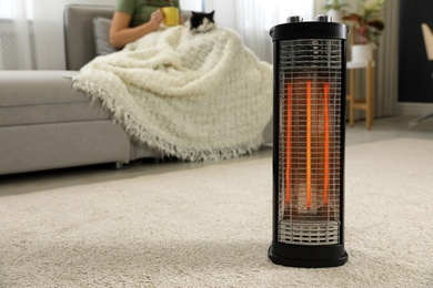 Woman with cat at home, focus on electric halogen heater, closeup