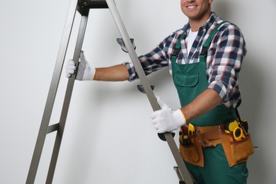 Professional builder with metal ladder on light background, closeup