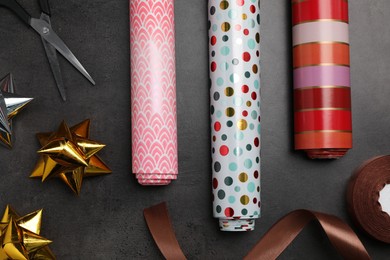 Different colorful wrapping paper rolls, satin ribbon, scissors and gift bows on grey table, flat lay