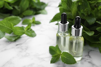 Photo of Bottles of mint essential oil and green leaves on white marble table, space for text