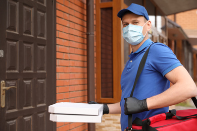 Courier in protective mask and gloves with pizza boxes near house entrance. Food delivery service during coronavirus quarantine