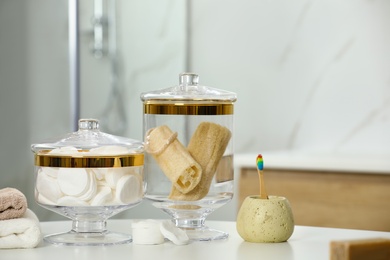 Composition of glass jar with cotton pads and luffa sponges on table in bathroom. Space for text