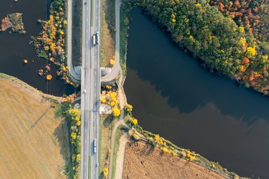Aerial view of road bridge across river near beautiful autumn forest