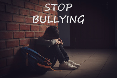 Message STOP BULLYING and sad little boy sitting on floor near brick wall indoors