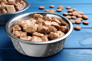Wet pet food in feeding bowl on blue wooden table, closeup