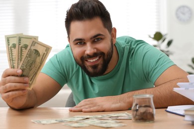Happy young man with money at wooden table indoors