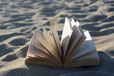 Photo of Open book on sandy beach, closeup view