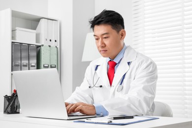 Doctor with laptop consulting patient at white desk in clinic. Online medicine