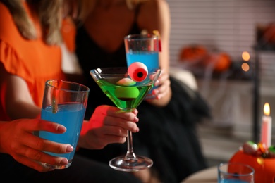Group of friends toasting with cocktails at Halloween party indoors, closeup