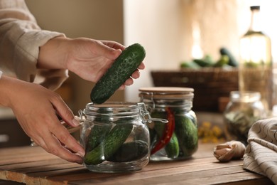 Woman putting cucumbers into jar at wooden table, closeup. Pickling vegetables