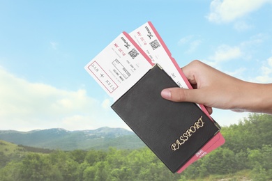 Woman holding passport with tickets in mountains, closeup. Travel agency service