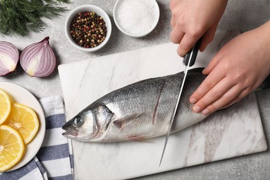 Photo of Woman cutting fresh raw sea bass fish at light gray table, closeup